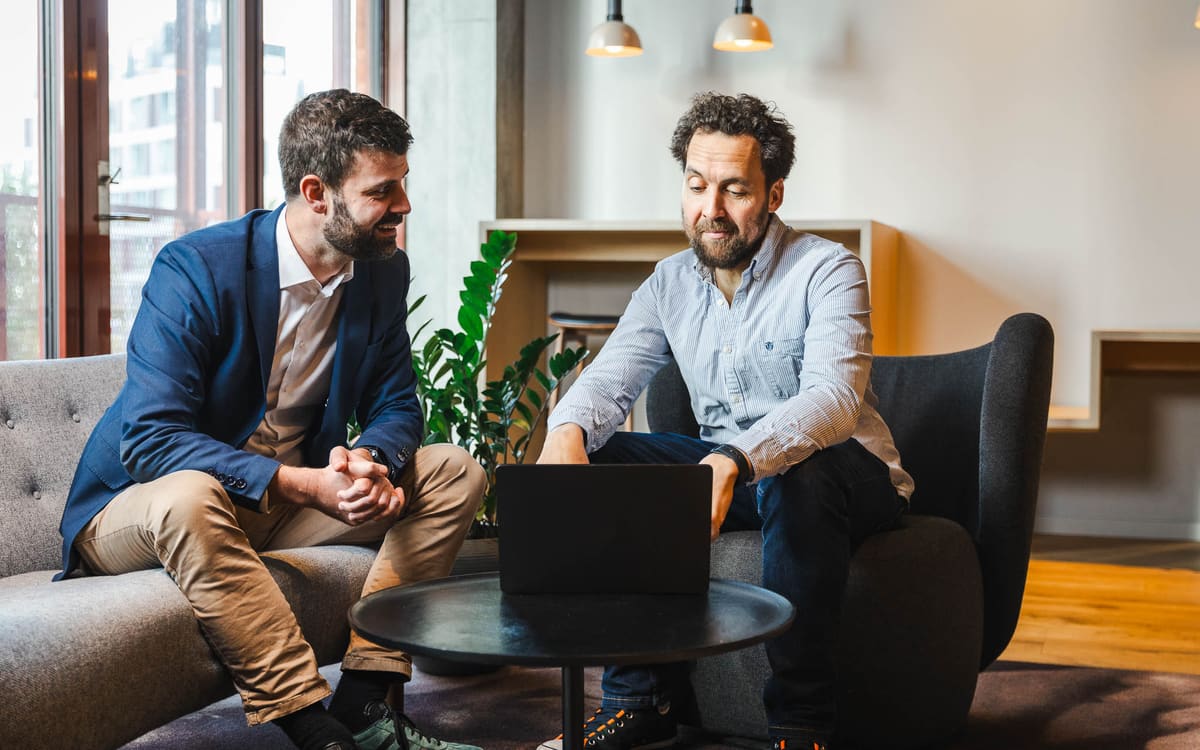 Jacob og Frederick gennemgår en opgave sammen på en laptop i et lyst mødelokale.